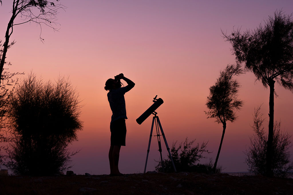 Man looking through binoculars at the sky at sunset