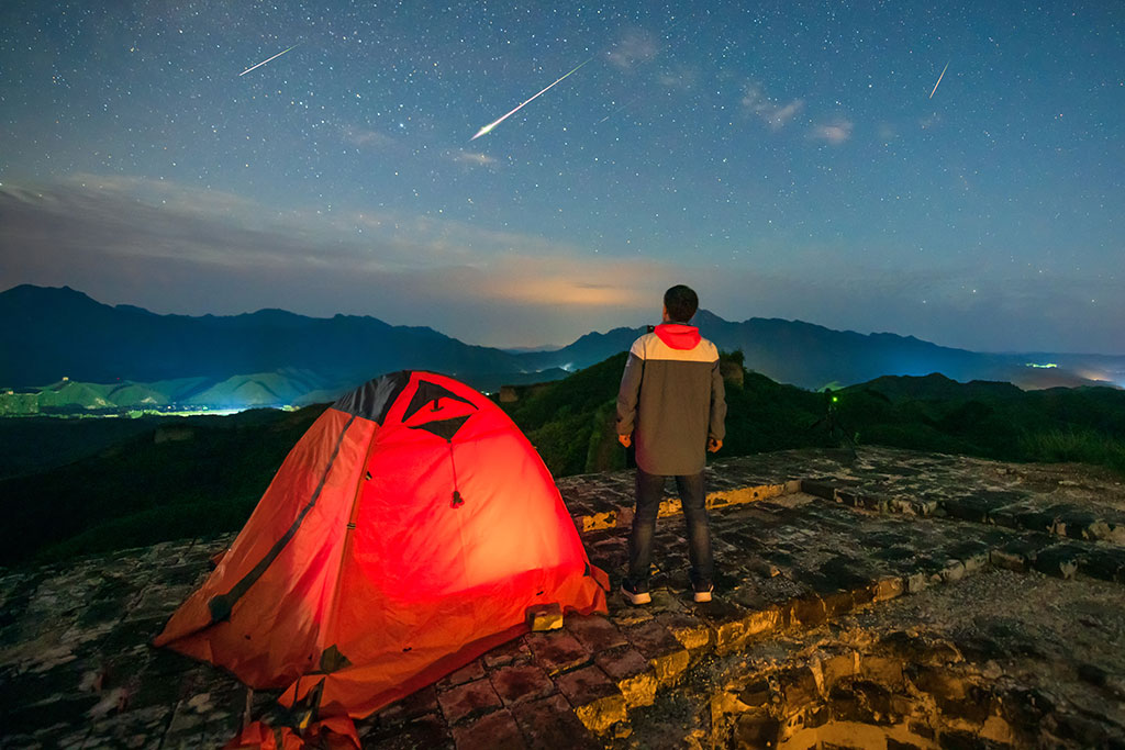 Man camping on a mountain watching meteor shower