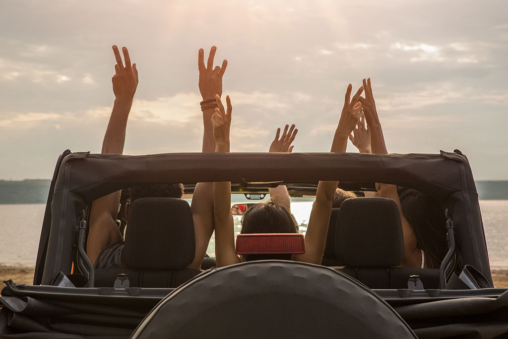 Young adults in a Jeep with their hands up through the open roof
