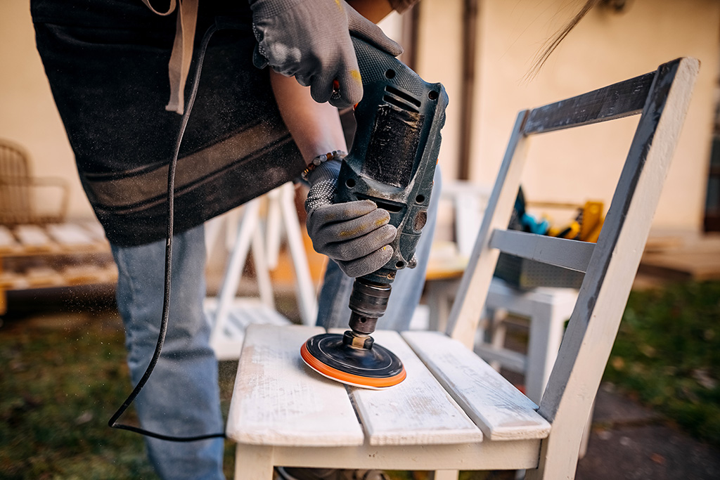 Man sanding an old wooden chair with a power sander