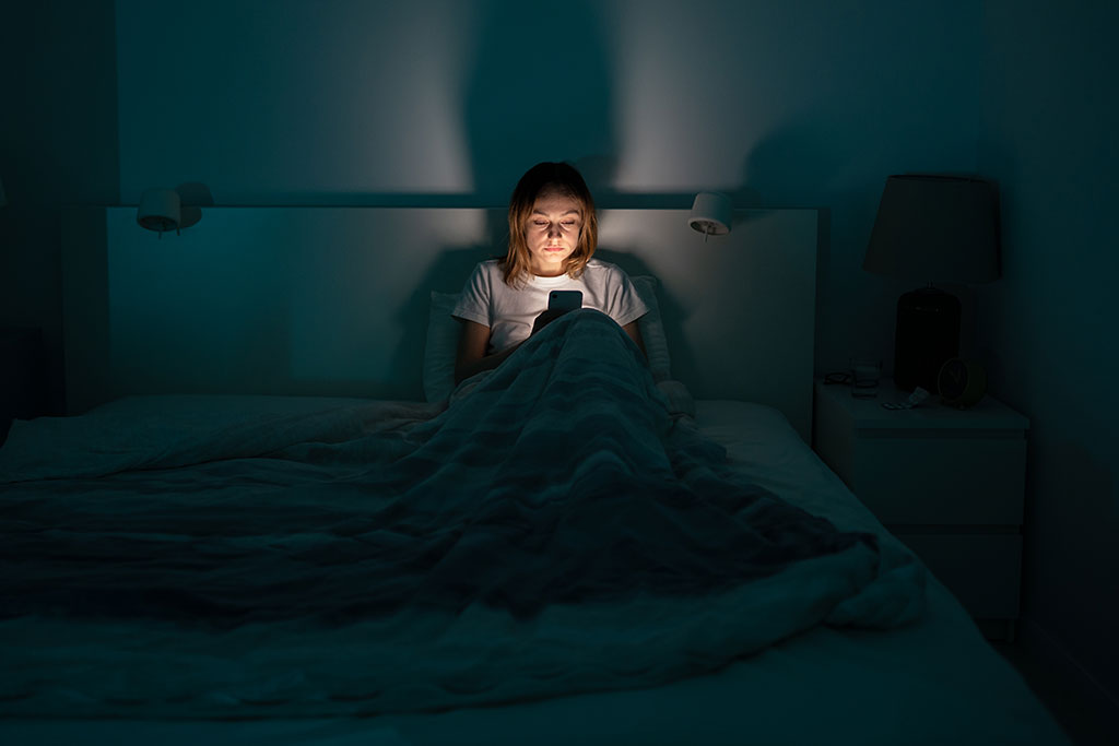 Young girl sitting in bed looking at her illuminated phone