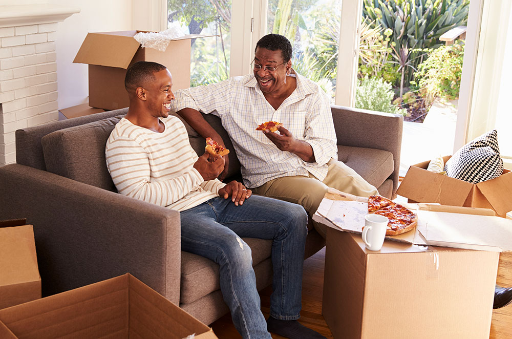 Father and son eating pizza surrounded by moving boxes.