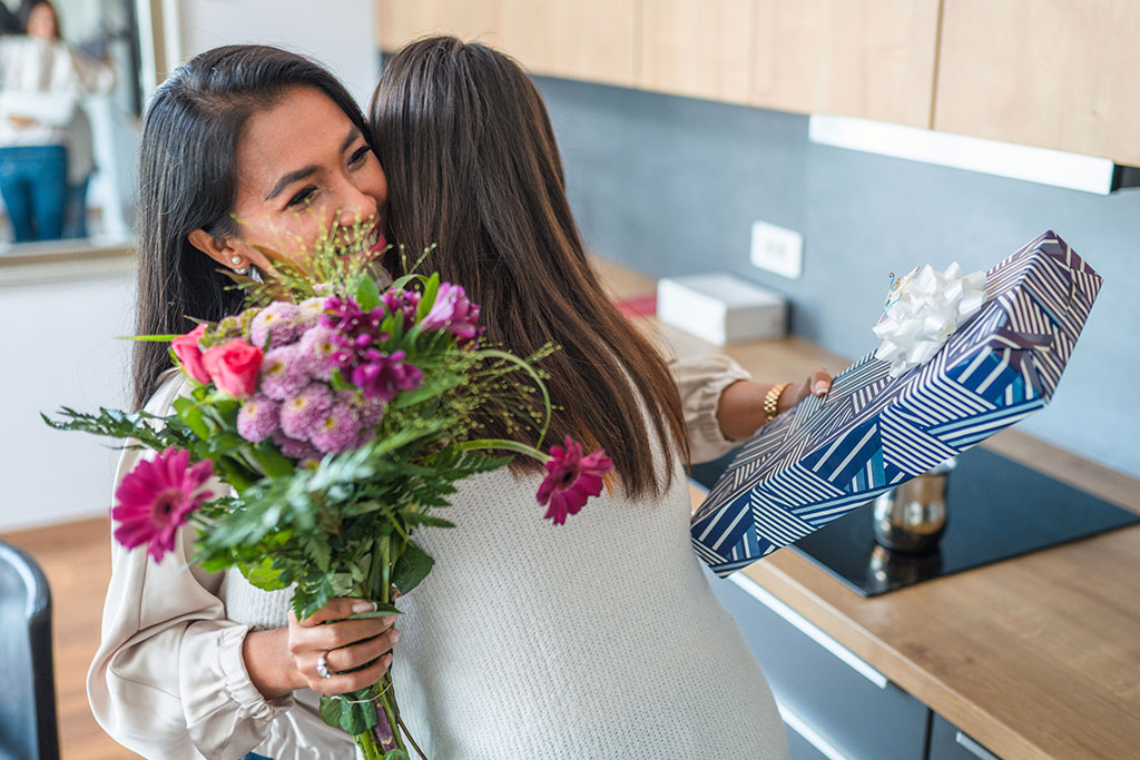 Daughter giving mom flowers and present