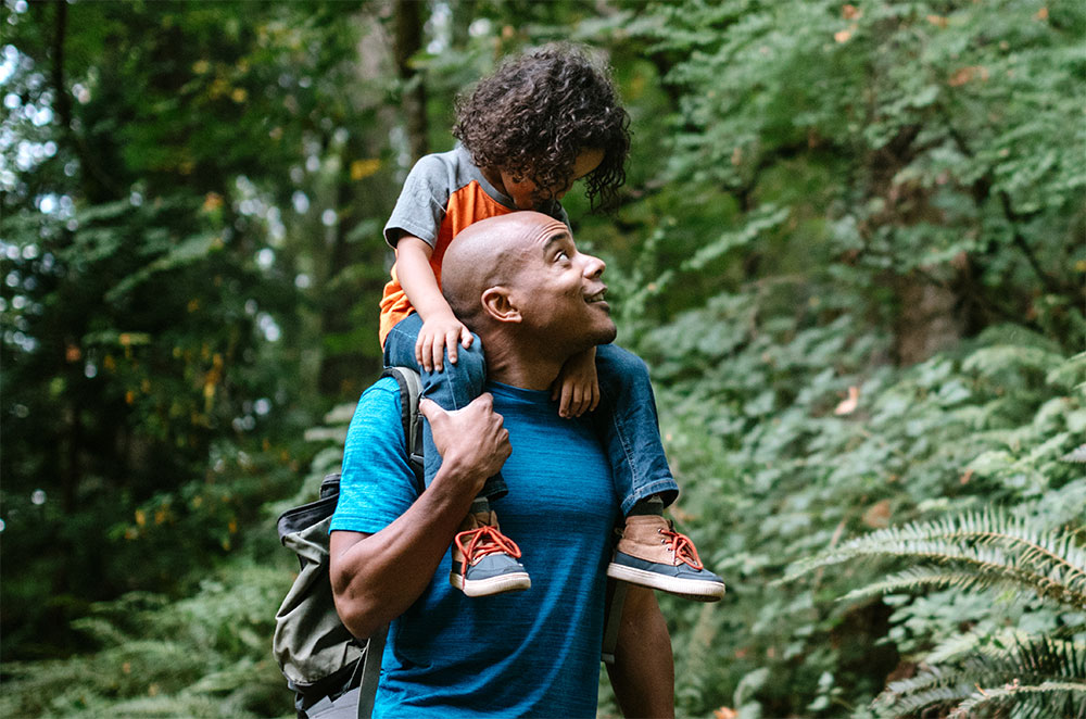 Son on dads shoulder hiking on trail