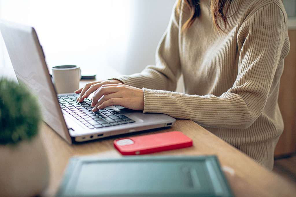 Woman working on laptop with phone face down to the side