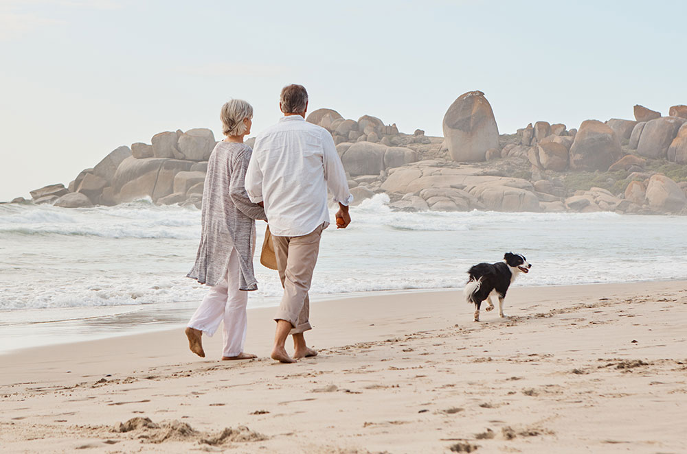 Older couple walking on beach with sand