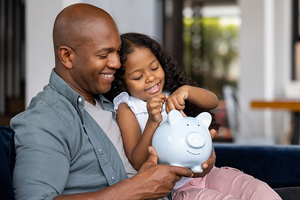 Dad and daughter putting money in piggy bank