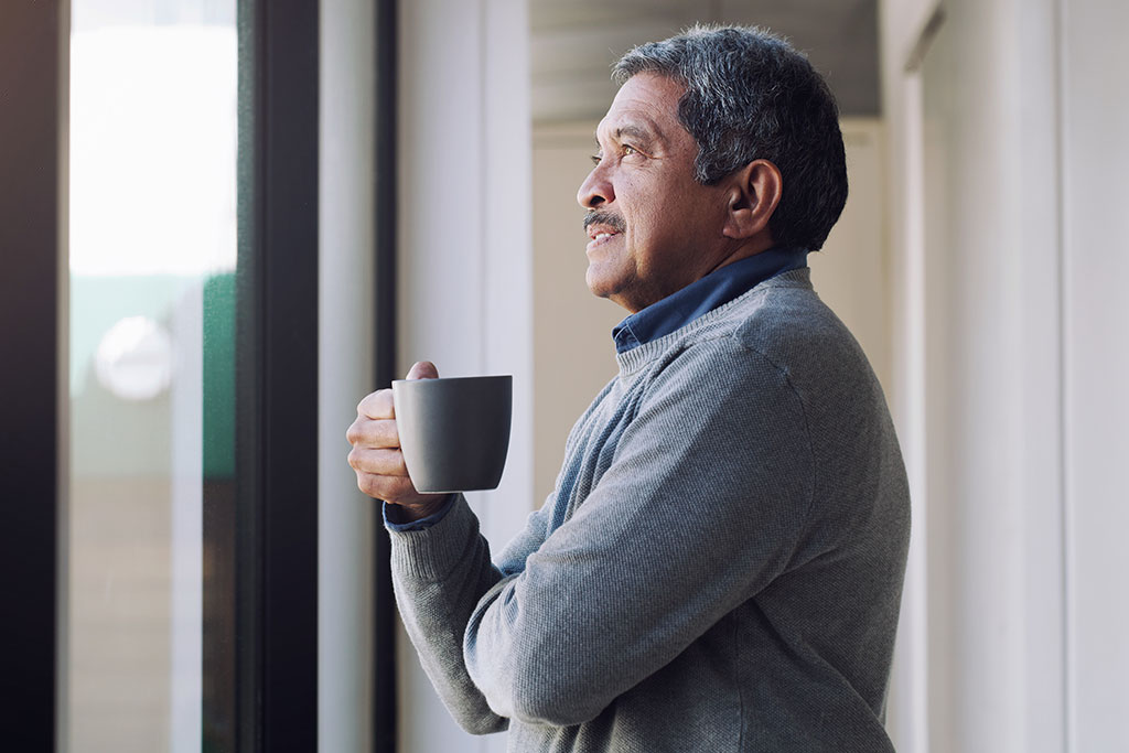 Older man holding mug looking out window