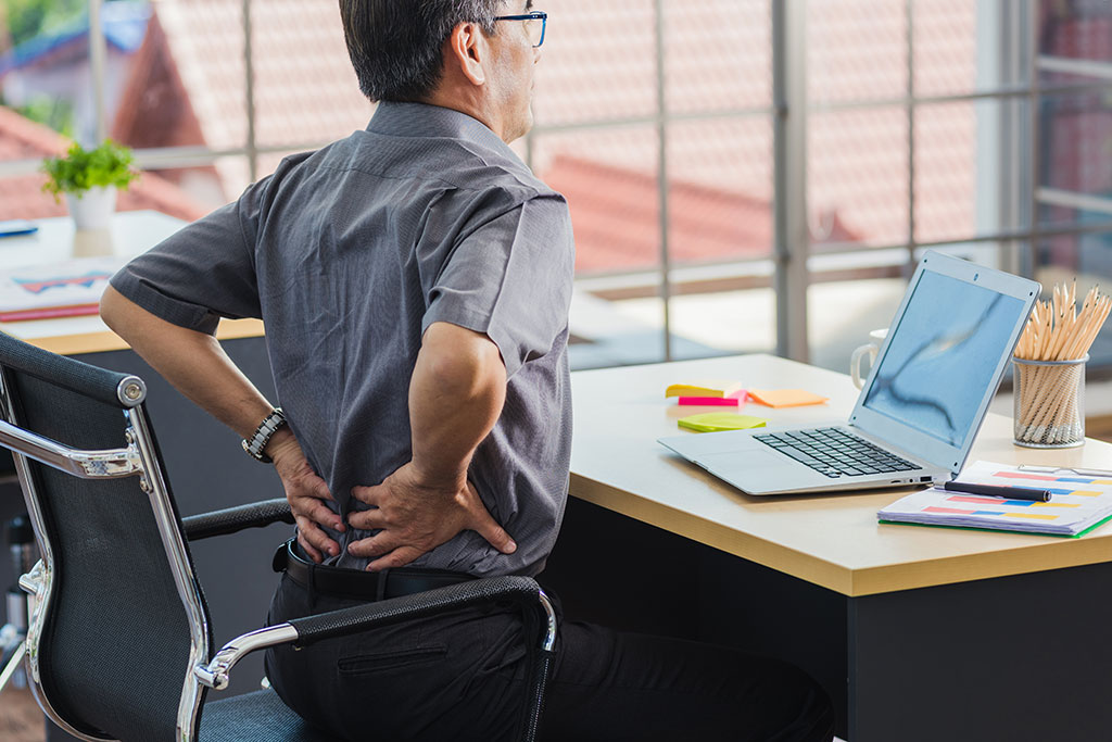 Person sitting at desk with hands on sore back