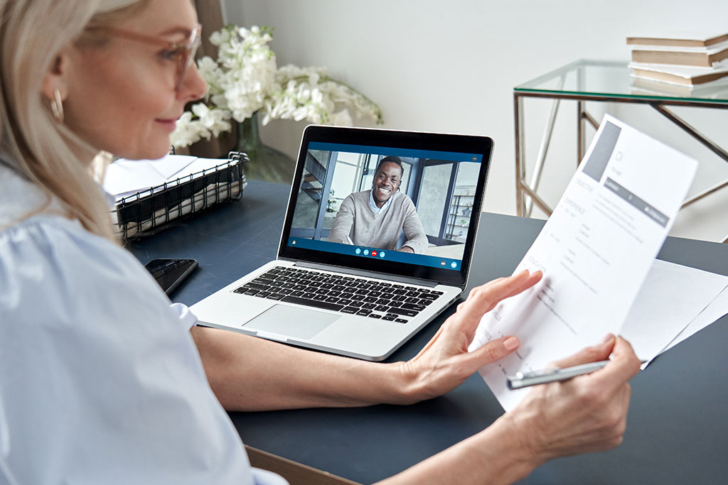 Business women looking at resume on video call interviewing young man