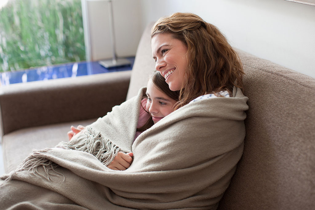 Mother and daughter on couch cuddling with blanket